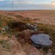 A damaged millstone rests next to the remains of a circular stone shelter, while modern turbines spin away to the south. Photo by Barney Devine.