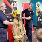 Damian McCaffrey and Michael Cullinan (NIFRS West) helping a primary school student try on a fire fighters' fire suit